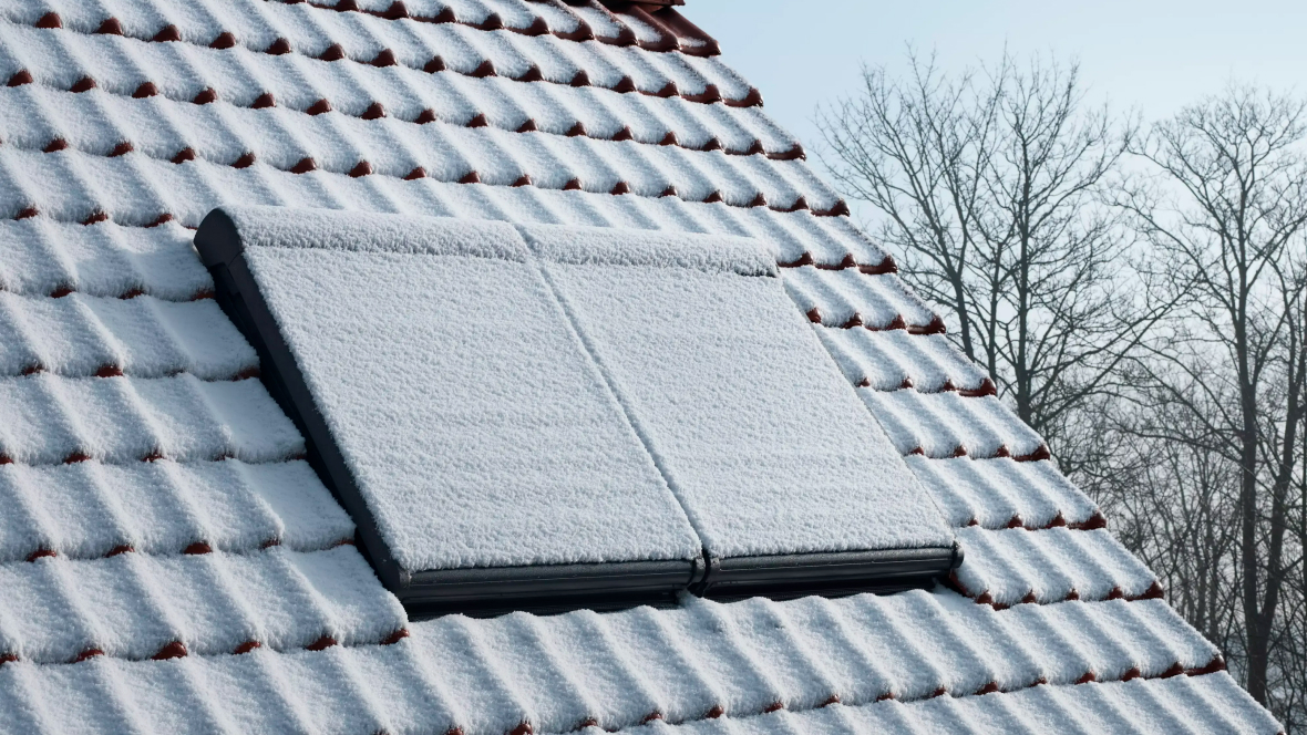 Vista esterna del tetto di una casa ricoperto di neve con due finestre VELUX con tapparelle abbassate